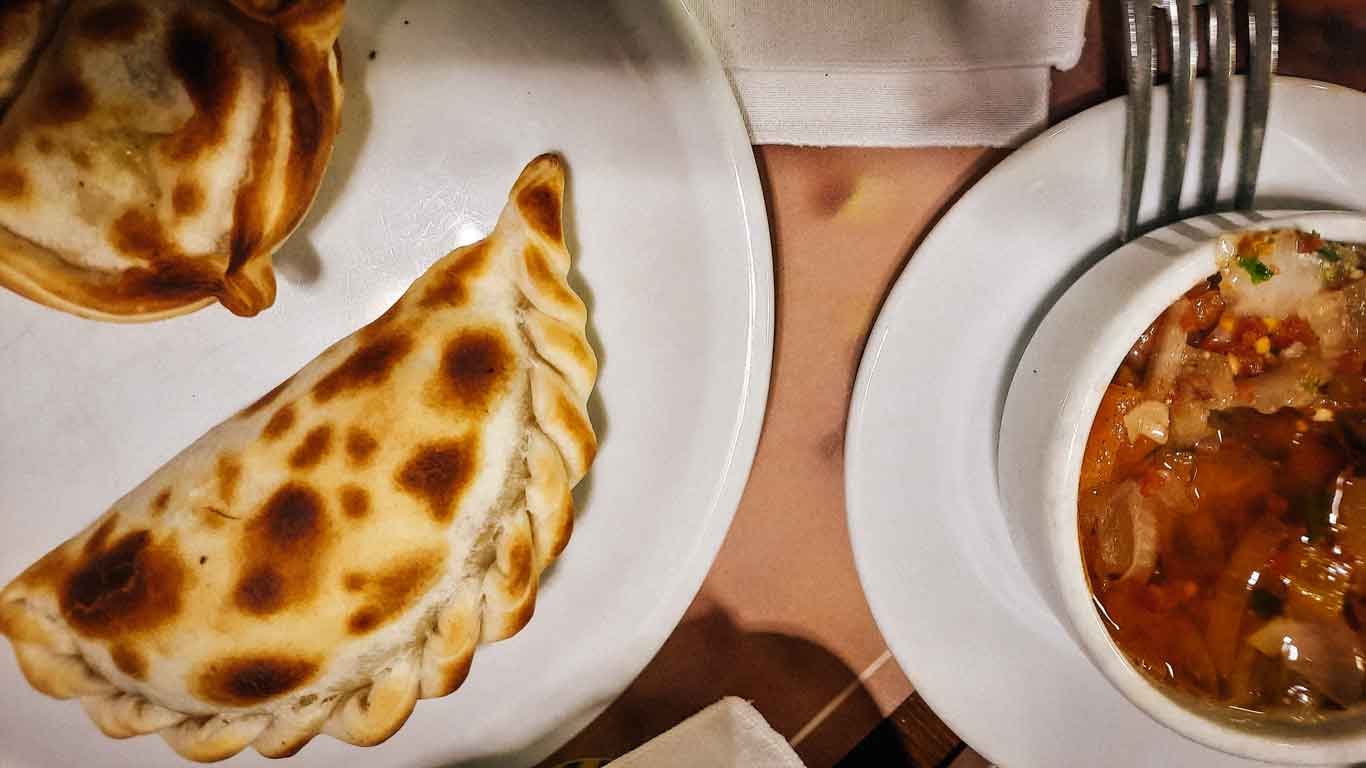 Close-up of a traditional Uruguayan empanada with a golden, toasted crust next to a bowl of savory vegetable stew, representing the rich culinary culture of Uruguay.