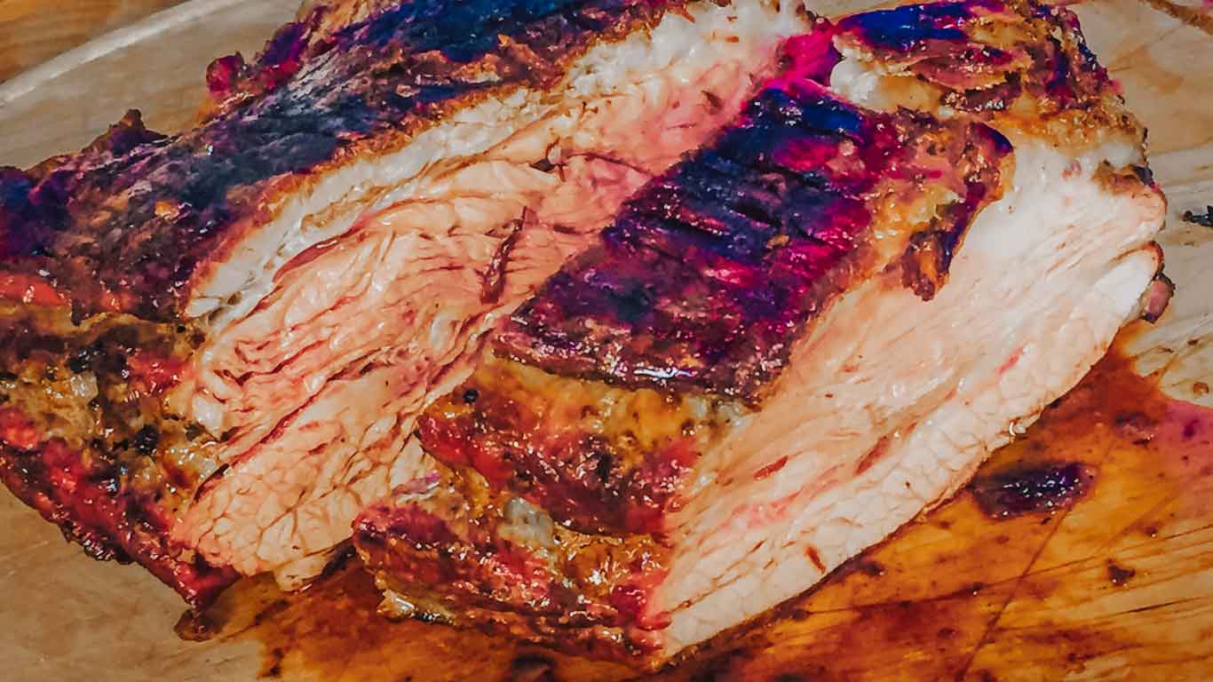 Succulent slices of grilled beef glisten on a wooden cutting board, showcasing the rich, charred crust characteristic of traditional Uruguayan barbecue.