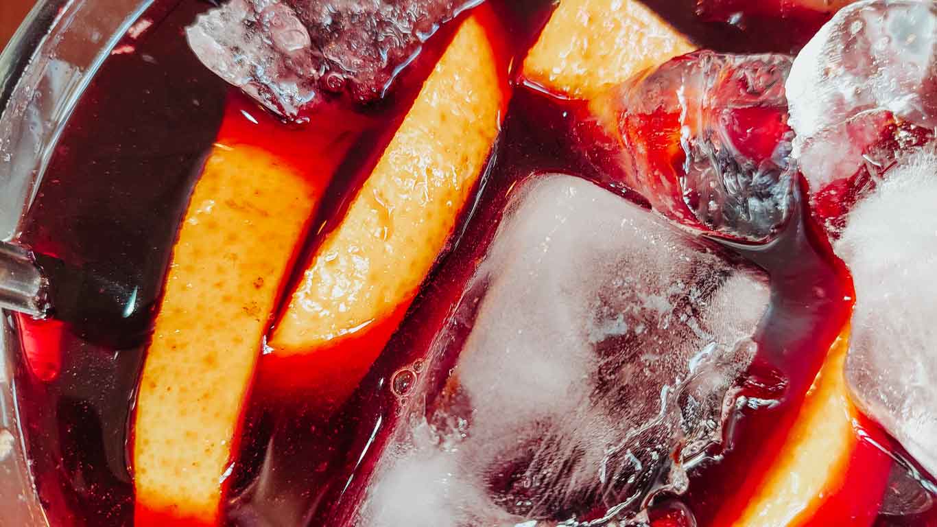 Close-up of a refreshing Uruguayan sangria, with vibrant slices of citrus fruit and glistening ice cubes submerged in a rich, ruby-red wine mixture, embodying a festive Uruguayan beverage experience."