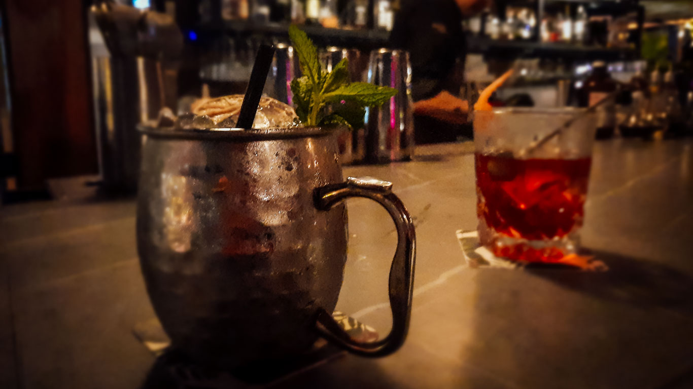 Two cocktails at a bar in Cartagena, featuring a Moscow Mule mug garnished with mint leaves and a lowball glass with a red drink. The background ambiance is cozy and intimate, perfect for enjoying a night out in the city.