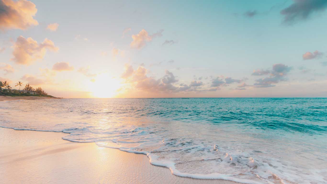 Paradisiacal beach in Hawaii at dawn, with the soft sunlight reflecting on the crystal-clear water and white sand. A few palm trees are in the background, framing the tranquil and serene scene.