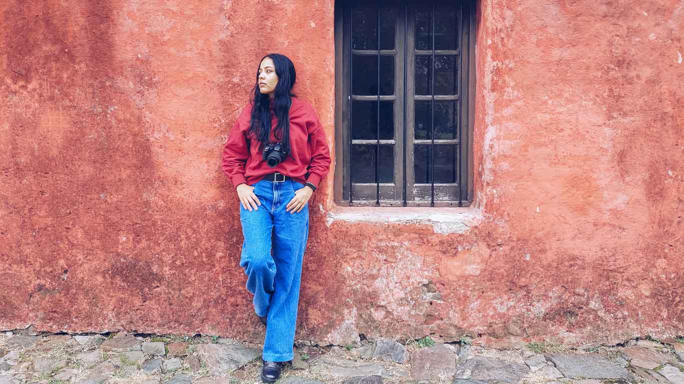 Woman leaning against a red wall, next to a window of the Museo Casa Portuguesa, in the Historic Center of Colonia del Sacramento.