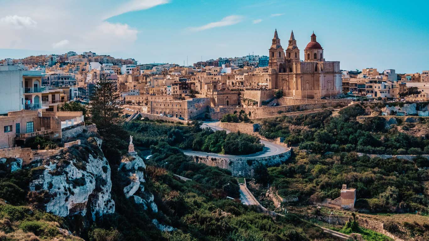 Panoramic view of a historic Maltese city with distinctive Mediterranean architecture, highlighting potential accommodation areas with a prominent church as a landmark. The city showcases excellent options for where to stay in Malta.