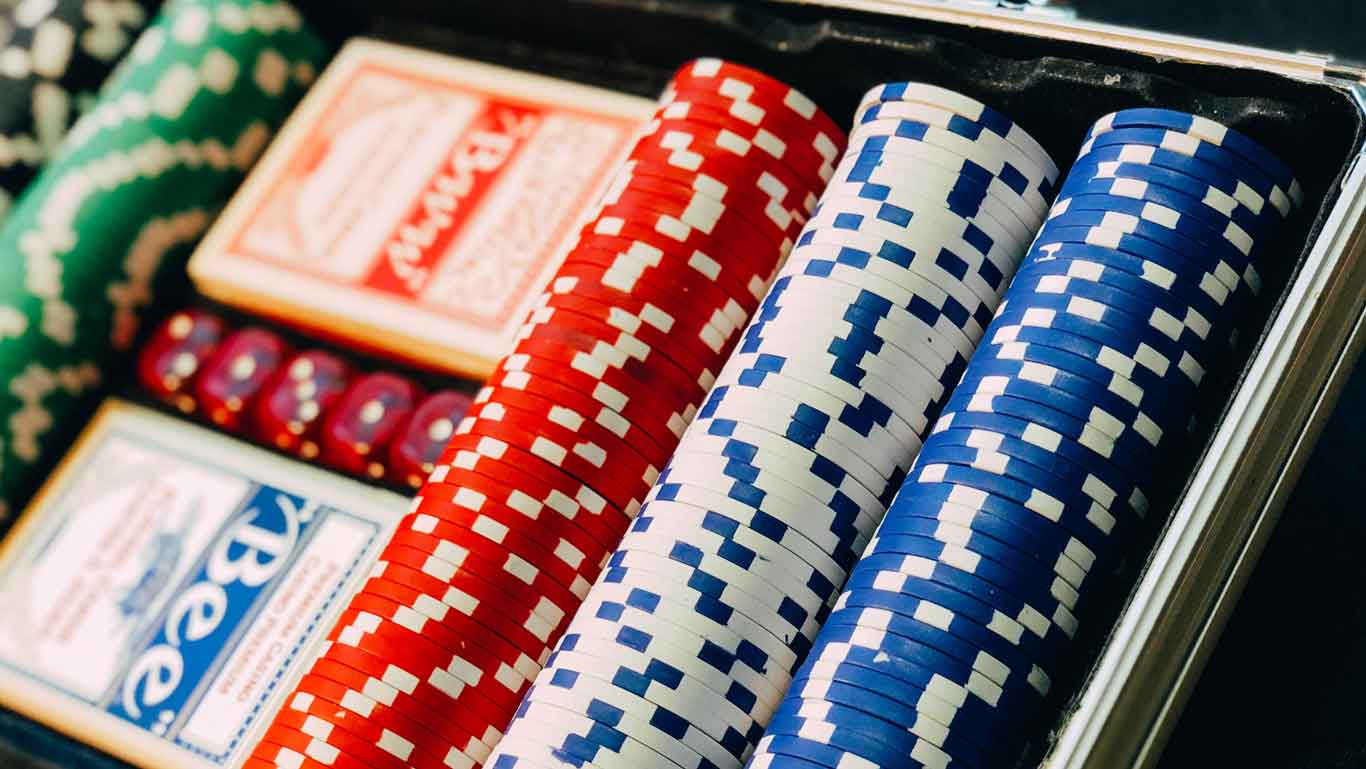 A close-up of poker chips and playing cards from a casino at Enjoy Punta del Este, an excellent tip on what to do in Punta del Este. The chips are stacked neatly in red, white and blue, accompanied by two decks of cards and a set of red dice.