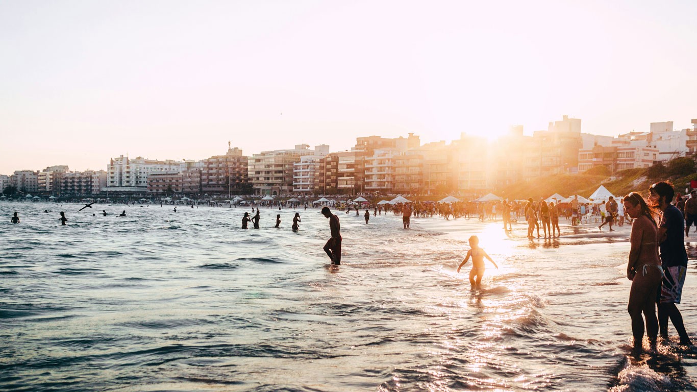 Praia do Forte in Cabo Frio at sunset, with buildings in the background and people walking towards the water.