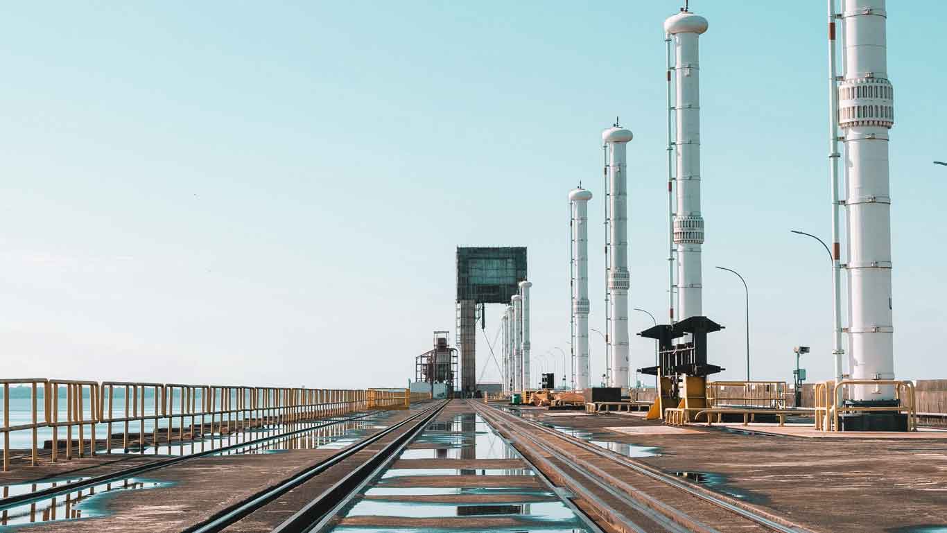 Panoramic view of the Itaipu Hydroelectric Power Plant in Foz do Iguaçu, showing multiple tall white hydroelectric towers lined up along a wet road reflecting the blue sky.