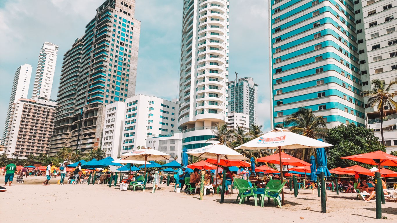 Bocagrande Beach in Cartagena. The beach has yellowish sand and is filled with beach umbrellas, with the modern buildings of the neighborhood in the background.