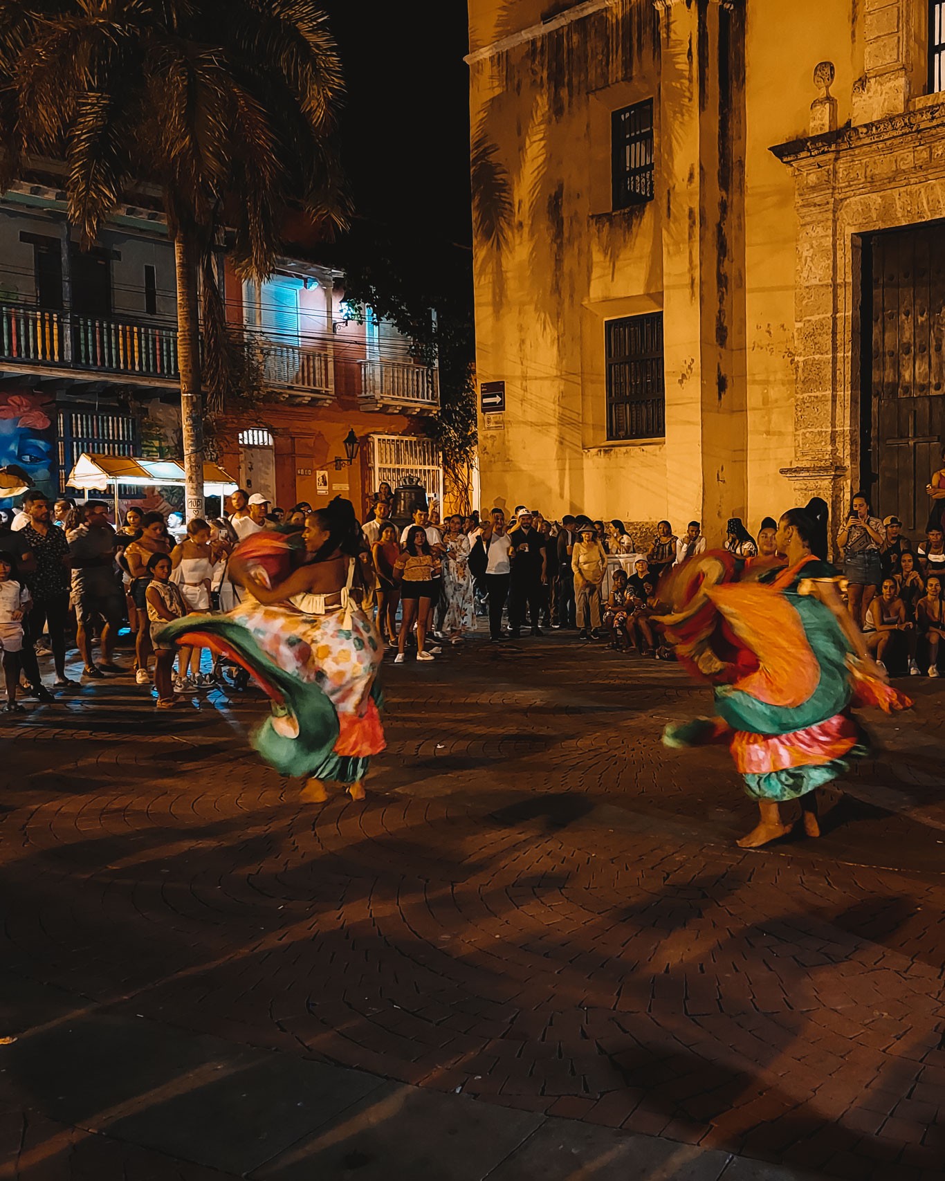 The Getsemaní neighborhood at night, with dancers wearing flowing, colorful Caribbean outfits, dancing through the neighborhood square.