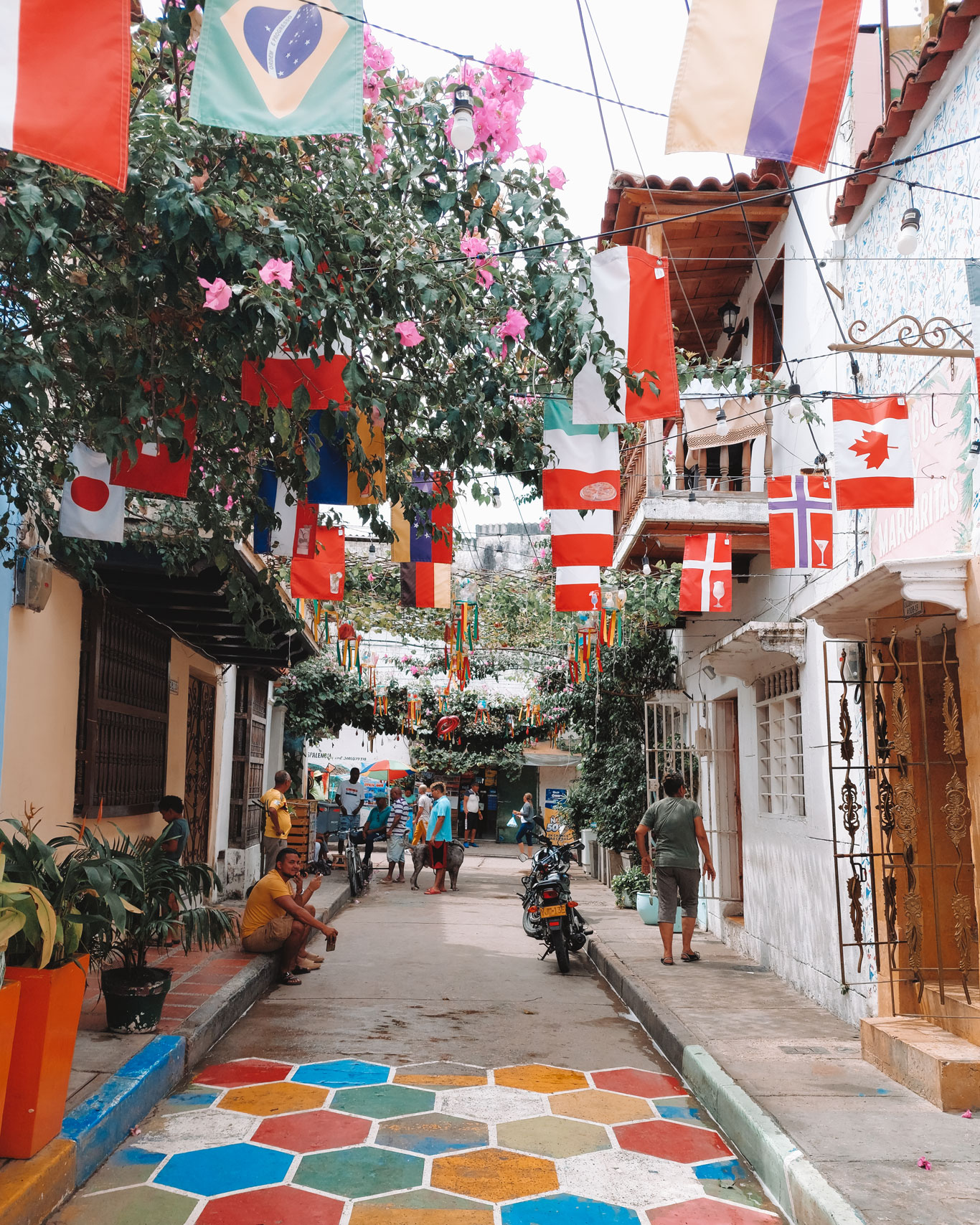 Narrow and colorful street in Getsemaní, one of the best options for where to stay in Cartagena de Indias. The street is covered with flags from various countries, and the ground is painted in multiple colors.