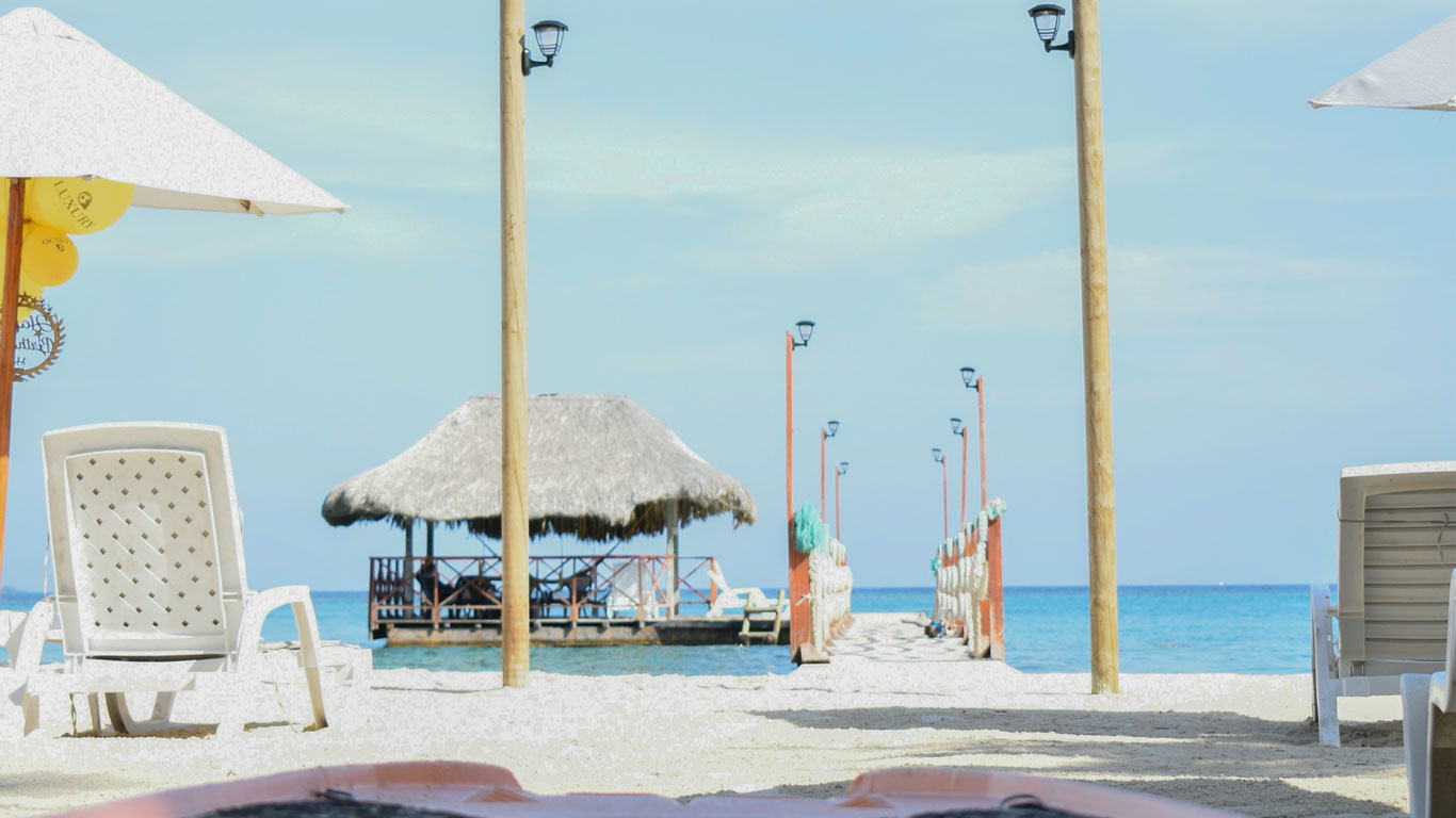 Entrance to the Luxury Beach Club resort in Islas del Rosario, Cartagena. In the foreground, there is a wooden pier with a covered tent at the end, and in the background, the blue sea merges with the sky.