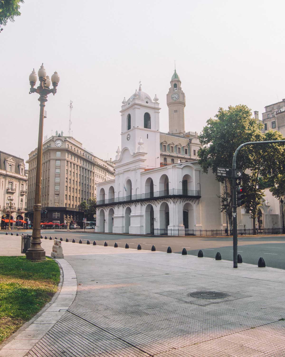 This image shows the Cabildo de Buenos Aires, a historic white colonial building in Plaza de Mayo. The Cabildo, with its arches and central clock tower, stands prominently in the foreground, while surrounding buildings reflect a blend of classic and modern architecture. The scene is peaceful, with an empty street and soft lighting, highlighting the iconic structure and its role in Argentine history. A vintage streetlamp and some greenery can be seen to the left, adding to the old-world charm of the area. This museum is a popular stop for visitors exploring cultural landmarks during their 3 days in Buenos Aires.