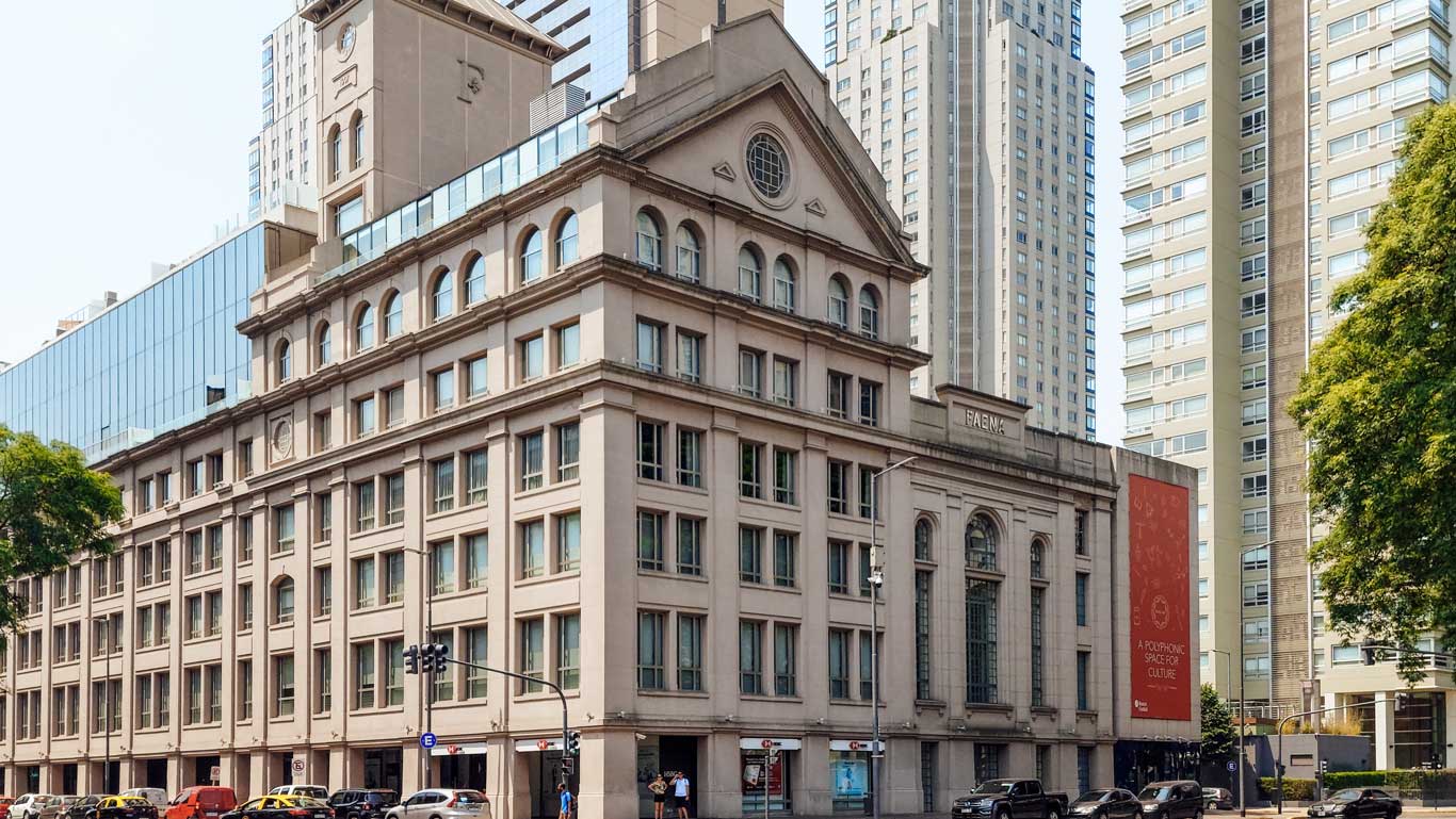 This image showcases the Faena Art Center in Buenos Aires, a neoclassical-style building surrounded by modern high-rise towers, highlighting the city's architectural charm. Known for its cultural and artistic significance, this area is a prime recommendation when considering where to stay in Buenos Aires, offering both luxury and proximity to urban attractions. The orange banner on the building adds a vibrant touch to the sophisticated cityscape.