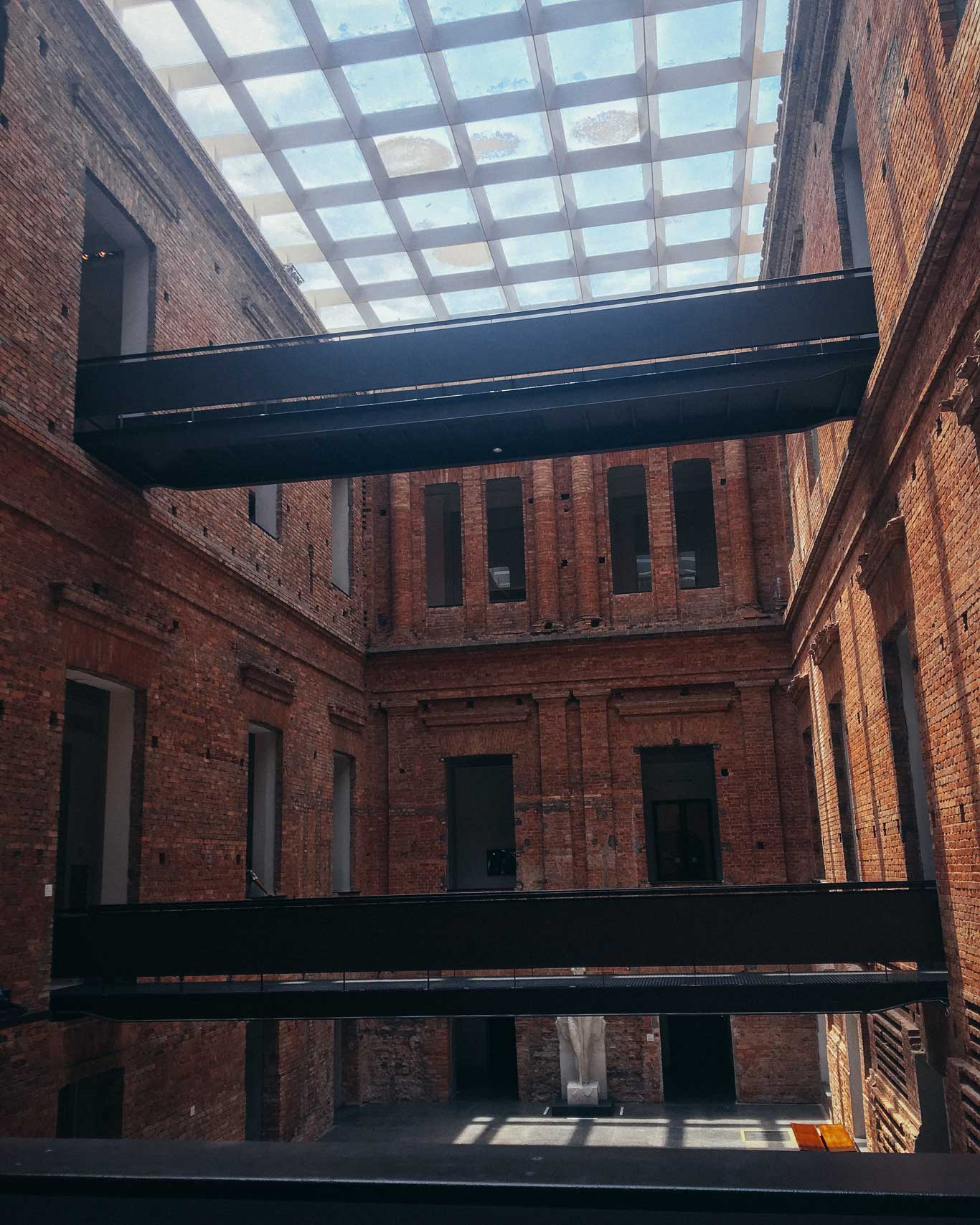 The interior of the Pinacoteca de São Paulo, showcasing its brick walls, modern metal walkways, and a skylight that floods the space with natural light.