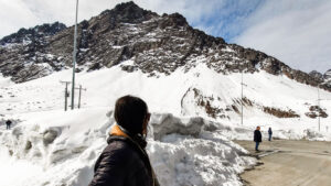 A traveler gazes at the snow-covered Andes Mountains during the snow season in Santiago, Chile, with rugged peaks and power lines cutting across the frosty landscape.