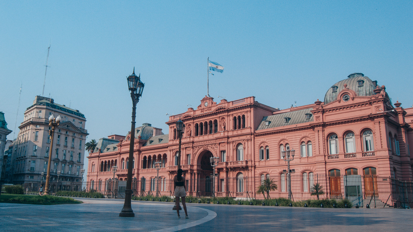 casa-rosada-buenos-aires Wide shot of the iconic pink Casa Rosada, the executive mansion and office of the President of Argentina, with a person standing in Plaza de Mayo admiring it.