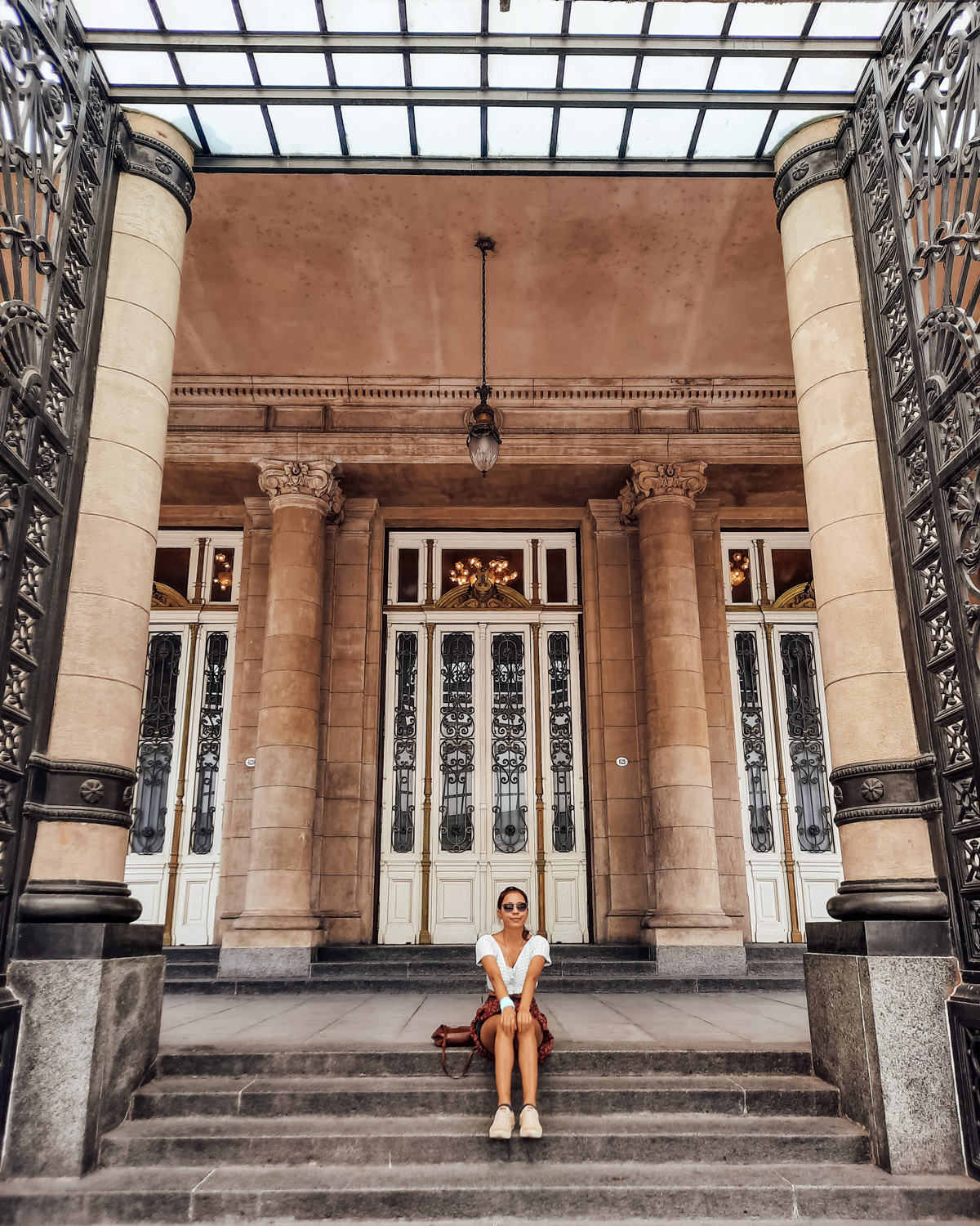 colon-theater-buenos-aires A visitor sits on the grand steps of Teatro Colón, framed by elegant iron gates and columns — experiencing the historic theater is one of the most iconic things to do in Buenos Aires.