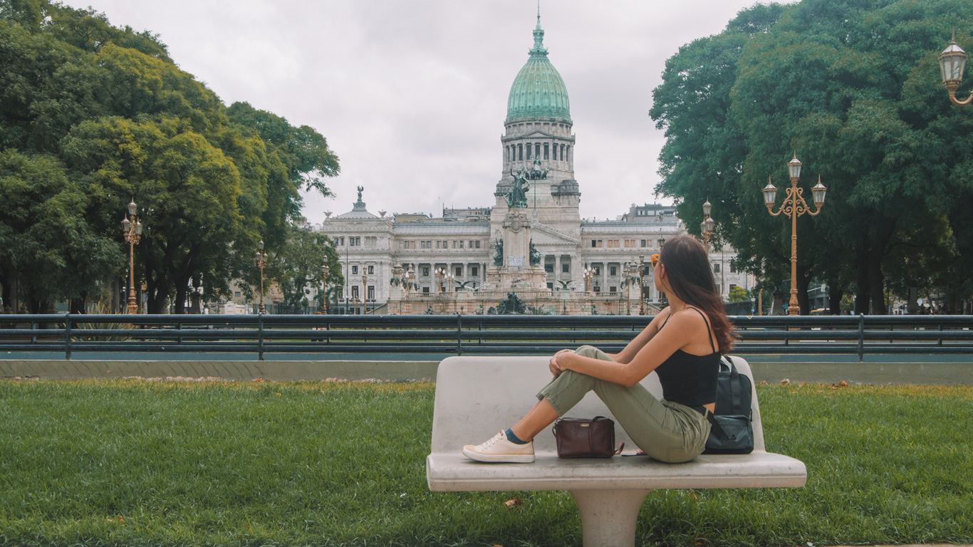 congress-square-argentina A woman relaxes on a bench facing the majestic Argentine National Congress building, surrounded by greenery and ornate lampposts