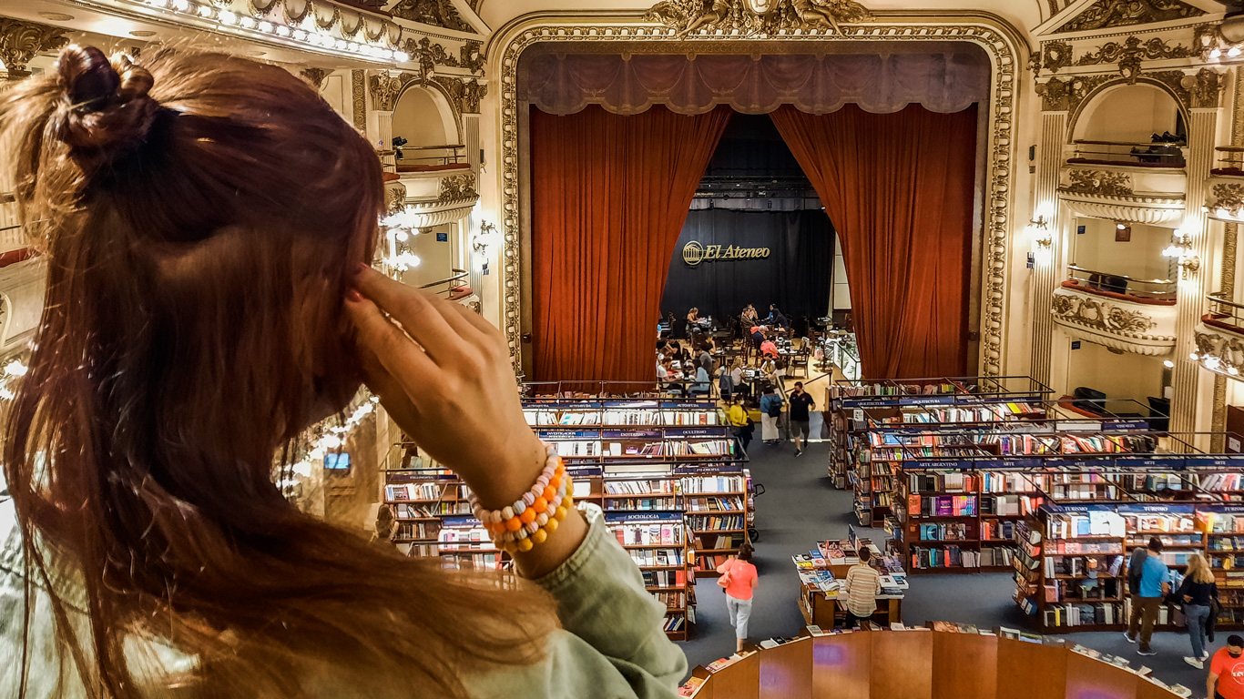 el-ateneo-buenos-aires A woman admires El Ateneo Grand Splendid, a famous Buenos Aires bookstore set in a converted theater, with red velvet curtains and ornate balconies.
