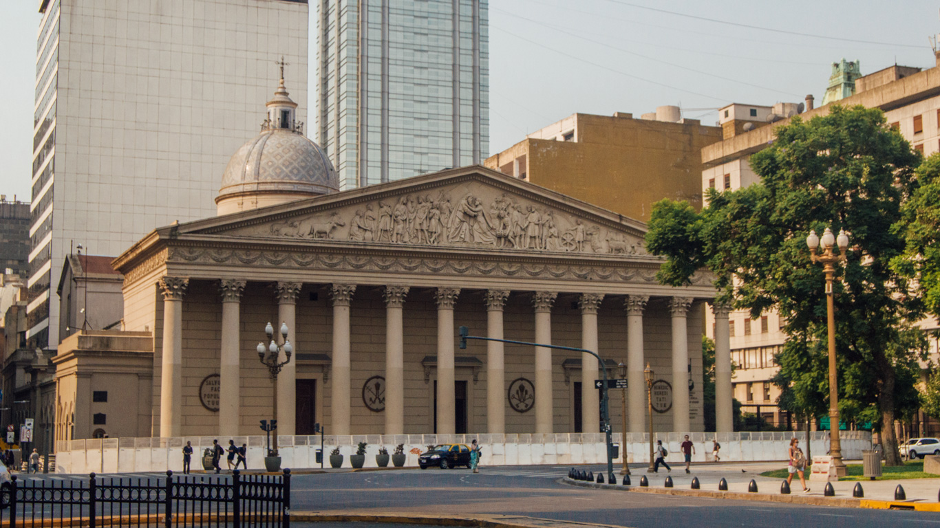 metropolitan-cathedral-of-buenos-aires Neoclassical facade of the Buenos Aires Metropolitan Cathedral with tall columns and detailed relief sculptures, standing out among modern downtown buildings.