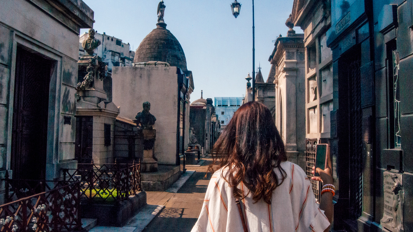 recoleta-cemetery-1 A woman walks through the narrow, ornate passageways of Recoleta Cemetery, surrounded by elaborate mausoleums.