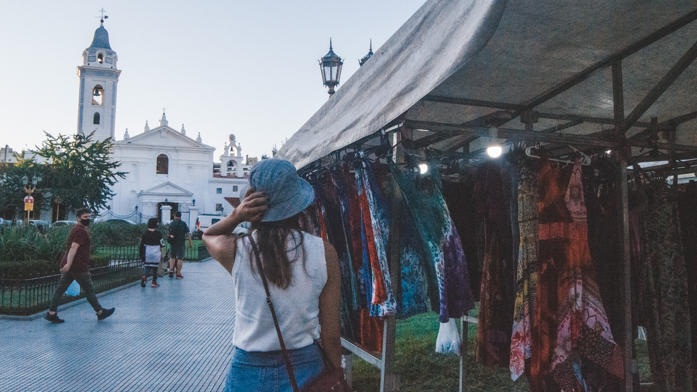 recoleta-street-market A woman browses colorful dresses at an outdoor market stall near the white façade of Basílica Nuestra Señora del Pilar.
