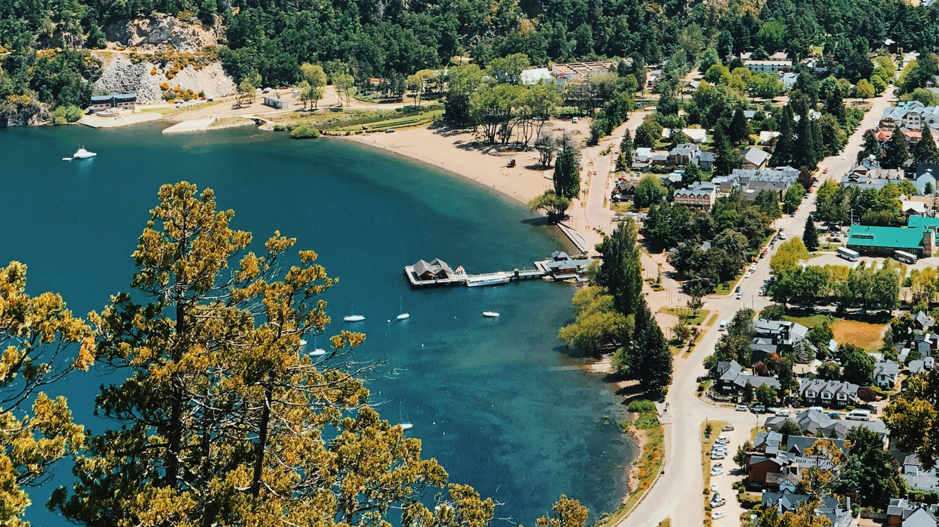 san-martin-de-los-andes Aerial view of San MartÃn de los Andes showing turquoise lake waters, a marina, and tree-lined streets, a serene destination on the way to snow in Bariloche.