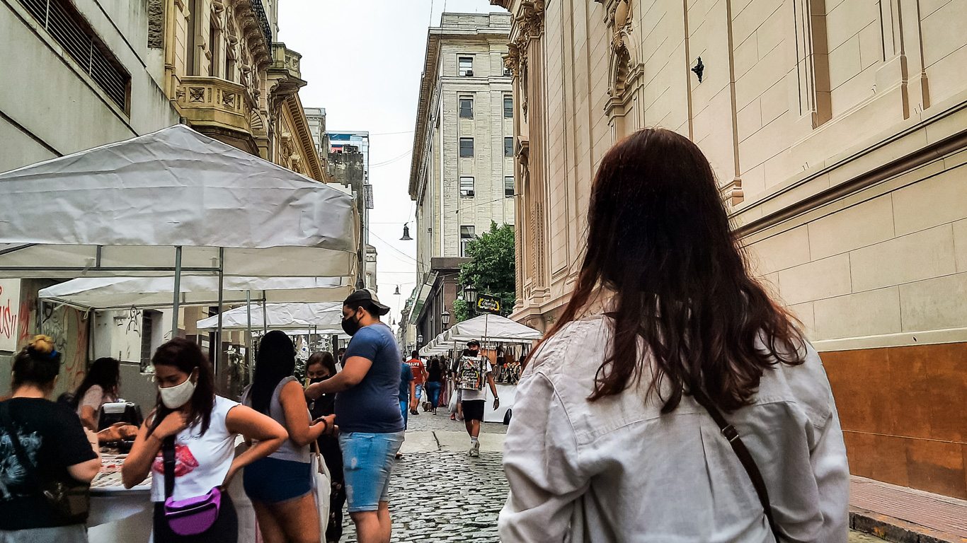 san-telmo-market A woman walking through a busy cobblestone street market in San Telmo, surrounded by locals and stalls, showcasing cultural must-dos.