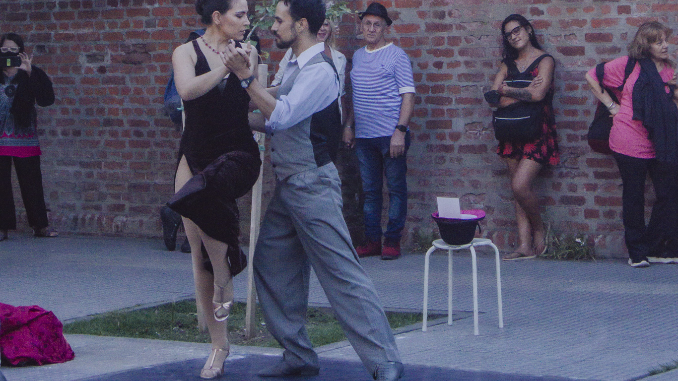 tango-show-in-buenos-aires A couple performs an intense tango dance outdoors against a brick wall backdrop, while a small group of people watches closely.