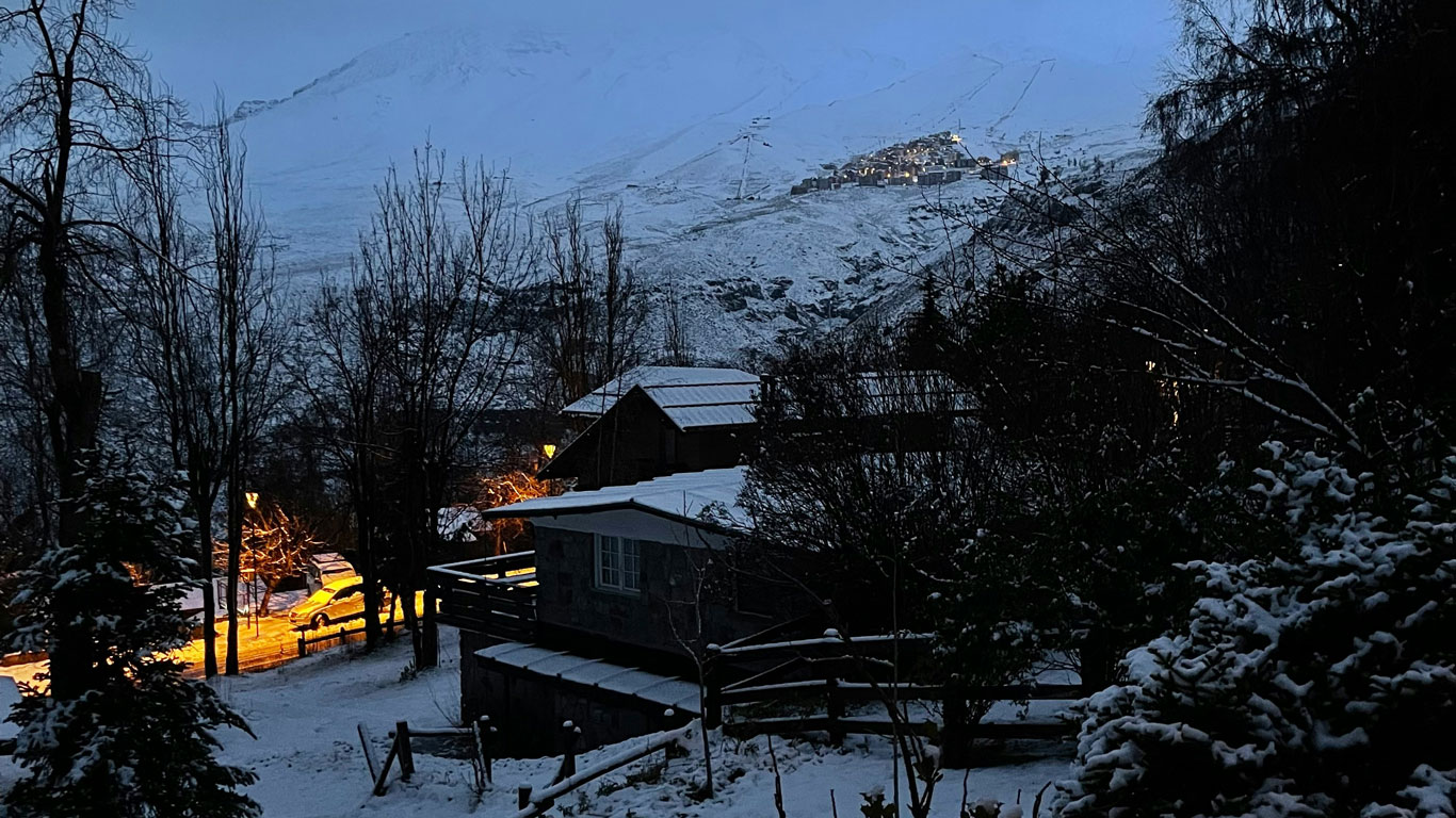 valle-nevado-chile Snow in Santiago creates a peaceful winter scene with cozy cabins and glowing lights nestled among snow-covered trees, with Valle Nevado village lit up in the background.