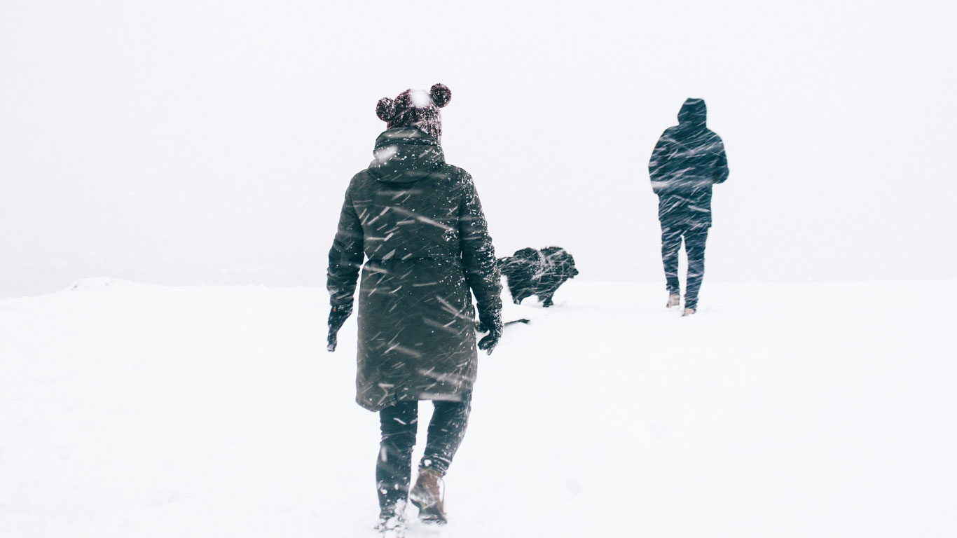 snow-season-ushuaia Three people walk through a snowy whiteout, bundled in heavy winter coats; one wears a beanie with pom-poms, braving the intense wind and falling snow. The visibility is low, capturing the raw and harsh beauty of winter in Ushuaia.