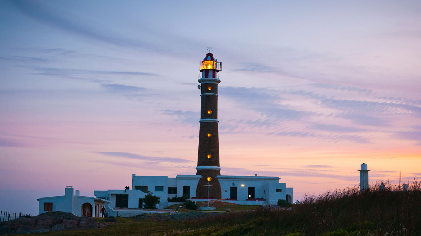 Iconic lighthouse glowing at dusk on the Uruguayan coast, backed by pastel skies and surrounded by modern white buildings. A scenic landmark often listed among the best places to visit in Uruguay.