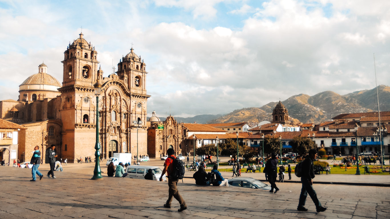 Tourists walking through Cusco’s vibrant Plaza de Armas with the iconic Cusco Cathedral in view and Andean mountains in the background.